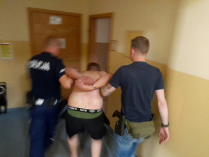dwaj policjanci prowadza zatrzymanego mężczyznę zakutego w kajdanki