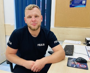 siedzący przy biurku funkcjonariusz w koszulce z napisem Policja
