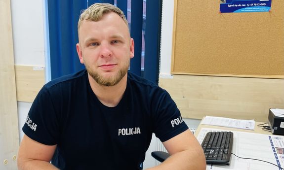 siedzący przy biurku funkcjonariusz w koszulce z napisem Policja