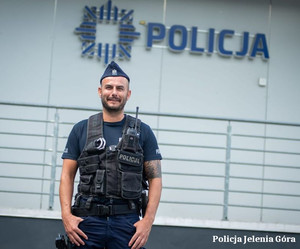 na pierwszym planie widać policjanta, w tle budynek z napisem policja