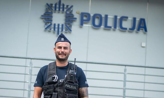na pierwszym planie widać policjanta, w tle budynek z napisem policja