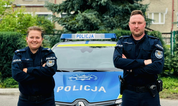 na zdjęciu umundurowani policjanci stoją przy radiowozie