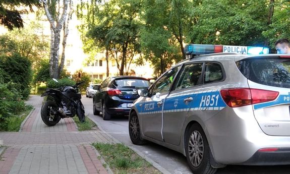 zaparkowany na chodniku motocykl, z boku widać zaparkowane przy ulicy cywilne auto, a za nim policyjny radiowóz