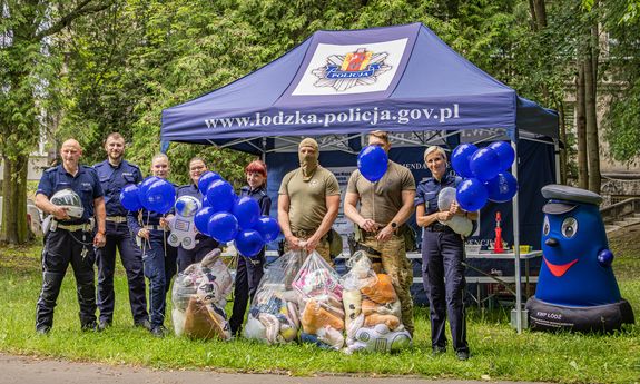 Policjanci w plenerze stoją pod namiotem niebieskim, obok balony