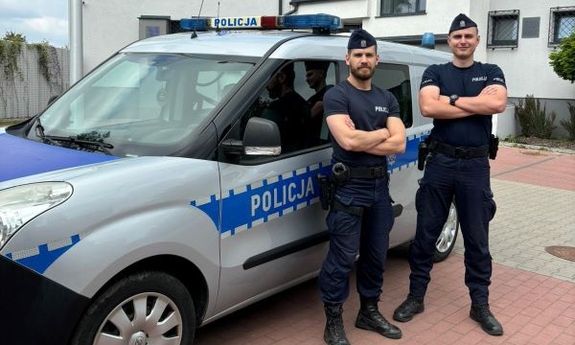 na zdjęciu dwóch umundurowanych policjantów stoi przy radiowozie