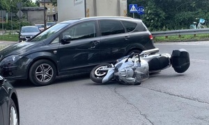 miejsce wypadku. Na drodze przy czarnym samochodzie leży porzewrócony motocykl. W głebi samochody na drodze