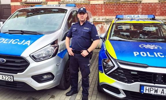 umundurowany policjant stoi pomiędzy dwoma radiowozami