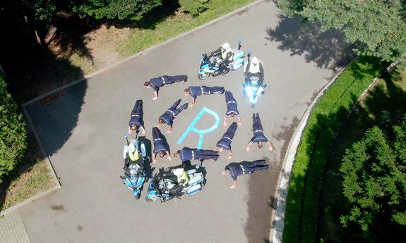 kadr z drona. policjanci robią pompki, obok stoją motocykle w nowym oznakowaniu, na środku literka R