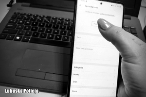 Telefon w dłoni. W tle laptop