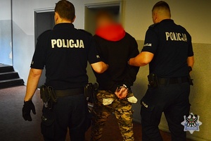 dwóch policjantów odprowadza mężczyznę w kajdankach założonych na ręce trzymane z tyłu
