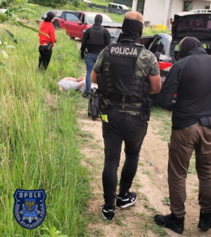 Zdjęcie przedstawia kilka osób, jeden z nich ma na kurtce napis Policja