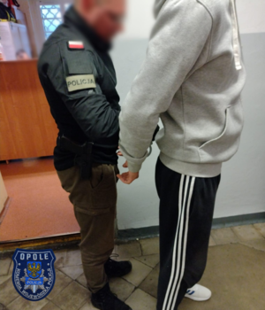 Zdjęcie przedstawia dwóch mężczyzn, jeden ma ręce skute z tyłu