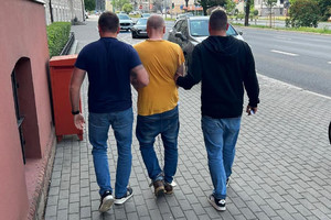 policjanci prowadzą zatrzymanego skutego kajdankami zespolonymi