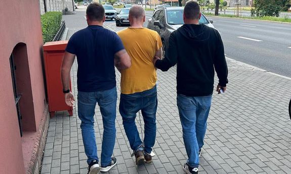 policjanci prowadzą zatrzymanego skutego kajdankami zespolonymi