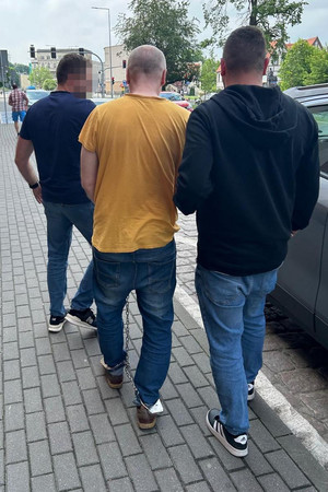 policjanci prowadzą zatrzymanego skutego kajdankami zespolonymi