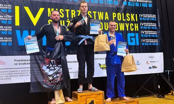 zdjęcie kolorowe przedstawiające st. post. Łukasza Banacha podczas stania na podium podczas zawodów ze złotym medalem