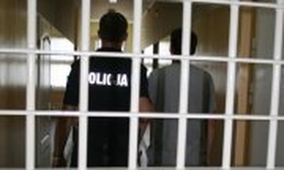 przez kraty widoczny policjant z zatrzymanym mężczyzną