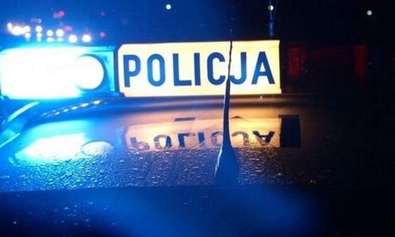 zdjęcie przedstawia fragment radiowozu z napisem Policja z włączonym światłem błyskowym w kolorze niebieskim