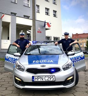 dwaj umundurowani policjanci stoją w otwartych drzwiach radiowozu, po jego lewej i prawej stronie