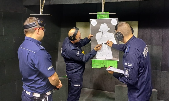 trzej policjanci na strzelnicy sprawdzają celność strzałów jednego z zawodników