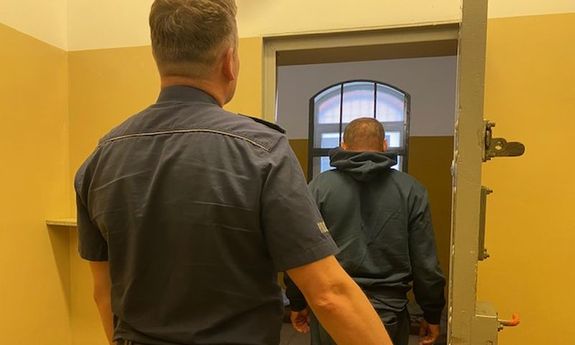 policjant stoi przed celą, w środku zatrzymany
