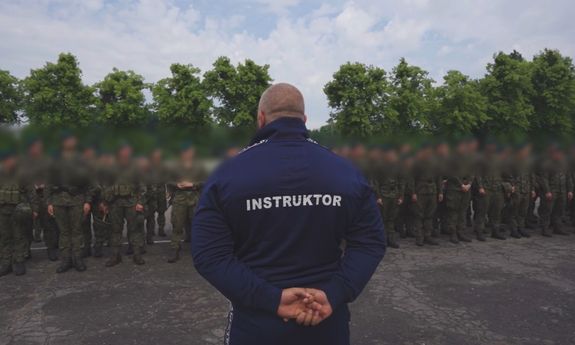 plecy policjanta z napisem instruktor, w tle żołnierze