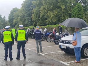 dwaj policjanci ruchu drogowego na parkingu, w tle uczestnicy rajdu