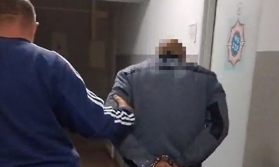 policjant po cywilnemu prowadzi zatrzymanego mężczyznę z założonymi kajdankami na ręce trzymane z tyłu