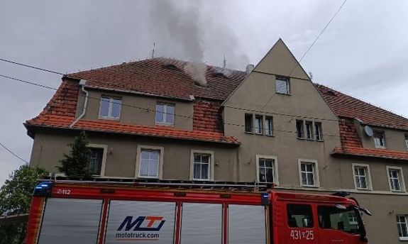 budynek mieszkalny z widocznym wydobywającym się z dachu dymem, a przed budynkiem samochód straży pożarnej