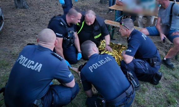 policjanci pochylają się nad kobietą i udzielają jej pomocy