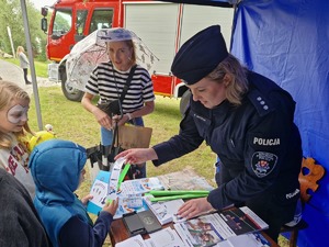 Policjantka z dziećmi w namiocie profilaktycznym, w tle wóz strażacki.