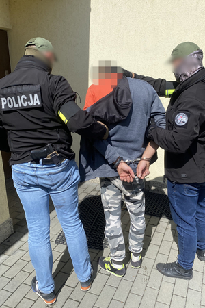 policjanci prowadzący zatrzymanego mężczyznę w kajdankach