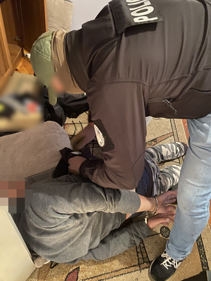 policjant pochylający się nad zatrzymanym mężczyzną leżącym na dywanie