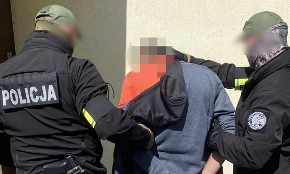 policjanci prowadzący zatrzymanego mężczyznę w kajdankach