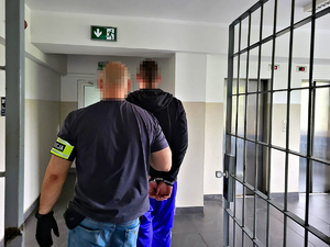policjant prowadzi zatrzymanego mężczyznę z kajdankami na rękach
