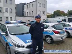 funkcjonariusz stoi na tle policyjnych radiowozów zaparkowanych na policyjnym parkingu