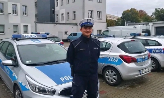 funkcjonariusz stoi na tle policyjnych radiowozów zaparkowanych na policyjnym parkingu