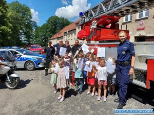 Policjantka pozuje do zdjęcia z grupą dzieci na tle wozu strażackiego.