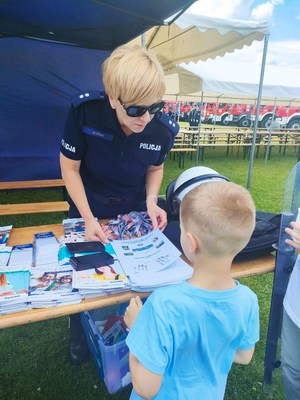 Policjantka przy stoisku profilaktycznym rozmawia z dzieckiem.