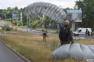 spadochroniarz ląduje na moście. obok patrzą na niego dwaj inni, którzy już wylądowali