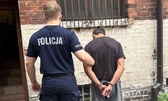 Na zdjęciu policjant trzymający mężczyznę w kajdankach