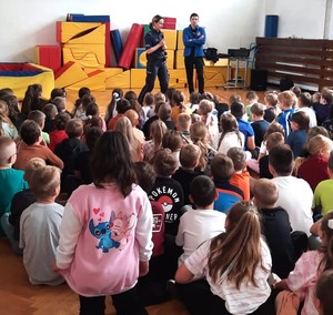 Policjantka i przedstawiciel Państwowej Stacji Sanitarno Epidemiologicznej rozmawiają z grupą dzieci.