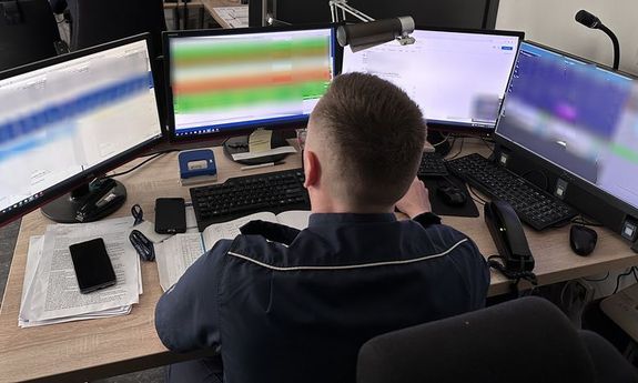 policjant siedzi przy biurku, stoi tam dużo ekranów z różnymi informacjami