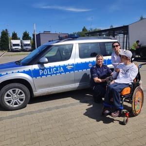 chłopiec na wózku przy policyjnym radiowozie w towarzystwie policjantki i mamy