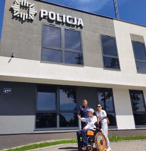 chłopiec na wózku przed budynkiem Policji, w towarzystwie umundurowanej policjantki i mamy