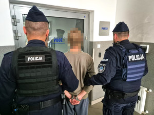 umundurowani policjanci prowadzą 22-latka, przed nimi drzwi do Pomieszczenia dla Osób Zatrzymanych