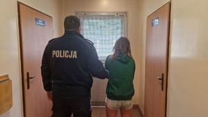 stojąca tyłem kobieta ubrana w krótkie spodenki i zielona bluzę zatrzymana przez policjanta w mundurze