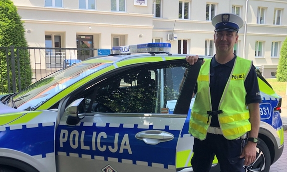 na zdjęciu umundurowany policjant stoi przy radiowozie