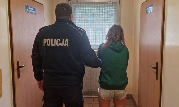 stojąca tyłem kobieta ubrana w krótkie spodenki i zielona bluzę zatrzymana przez policjanta w mundurze