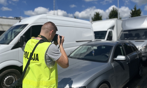 na zdjęciu policjant w żółtej kamizelce z napisem policja fotografuje odzyskane pojazdy